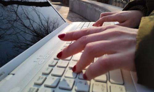 A person typing outdoors on a laptop.